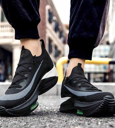 Black athletic shoes with green accents worn on a blurred street background