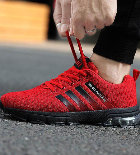 Red running shoe with black stripes being worn on a blurred background