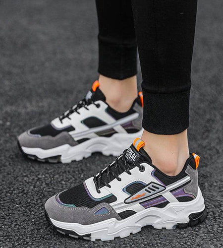 Person wearing black and gray sneakers with orange accents on a dark surface