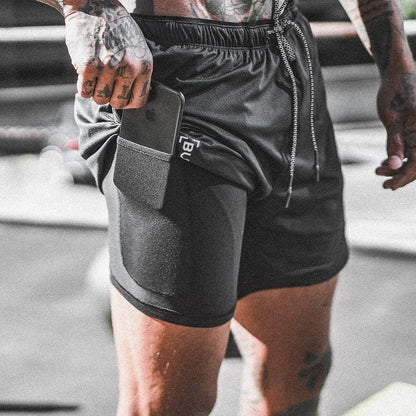 Person wearing black athletic shorts with a visible brand logo, standing on a blurred background.