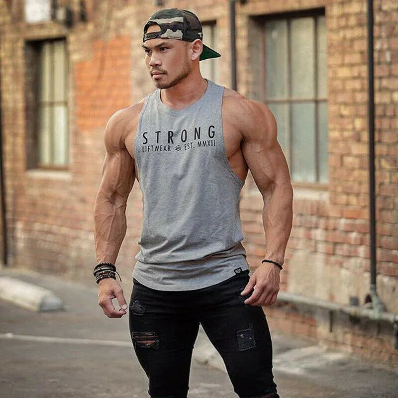 Muscular man wearing a gray tank top with 'STRONG' text, standing in an urban setting.