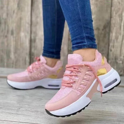 Pink sneakers with white soles worn by a person on a wooden floor.