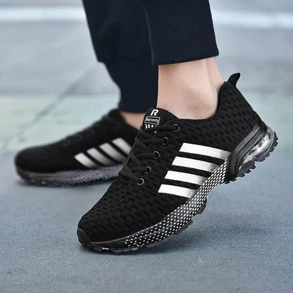 Black athletic shoes with white stripes worn on a blurred pavement background