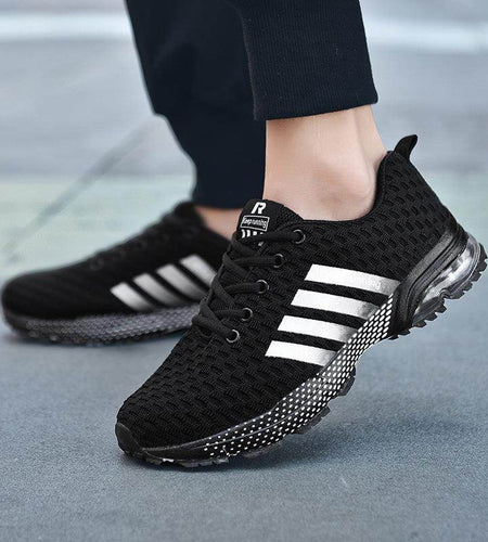Black athletic shoes with white stripes worn on a blurred pavement background