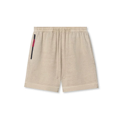 Beige shorts with a small black and red detail on a white background
