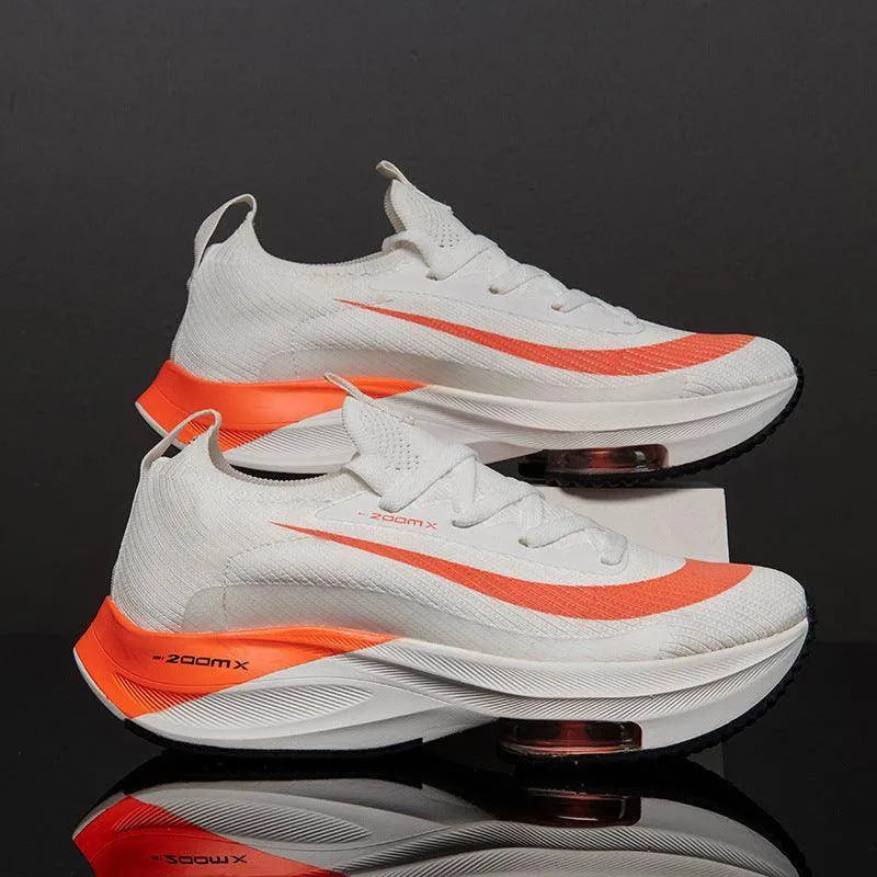 White and orange running shoes with 'zoom x' text on a reflective black surface.