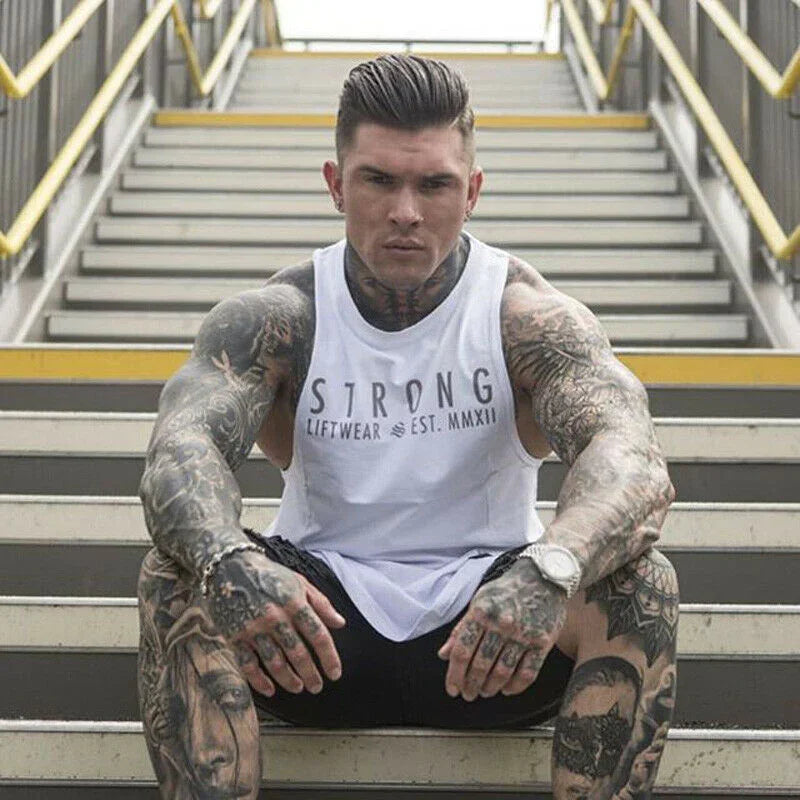Man with tattoos wearing a white tank top with 'STRONG' text sitting on stairs.