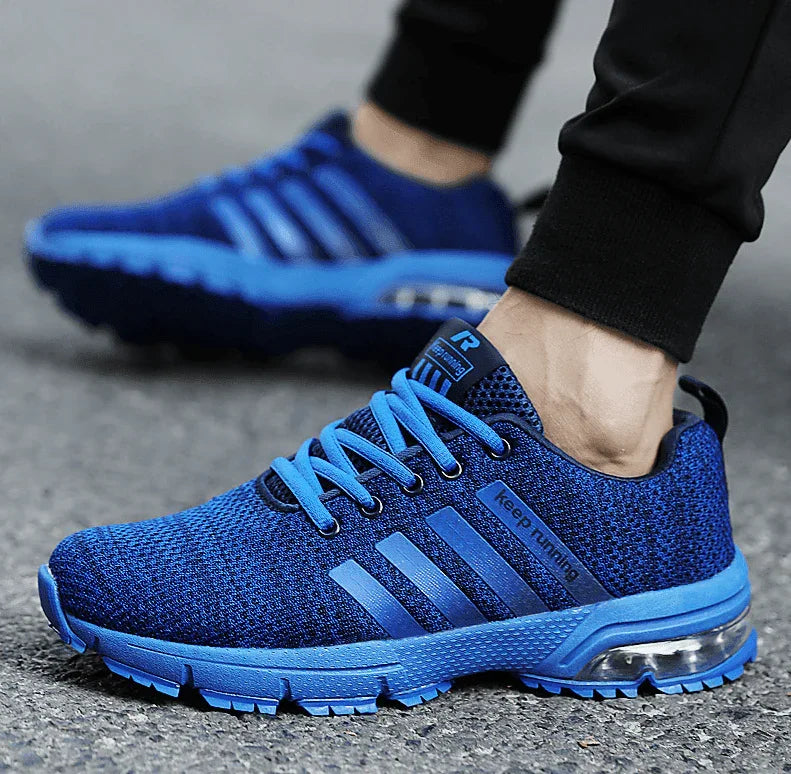 Blue athletic shoes with a brand logo worn by a person on a gray surface