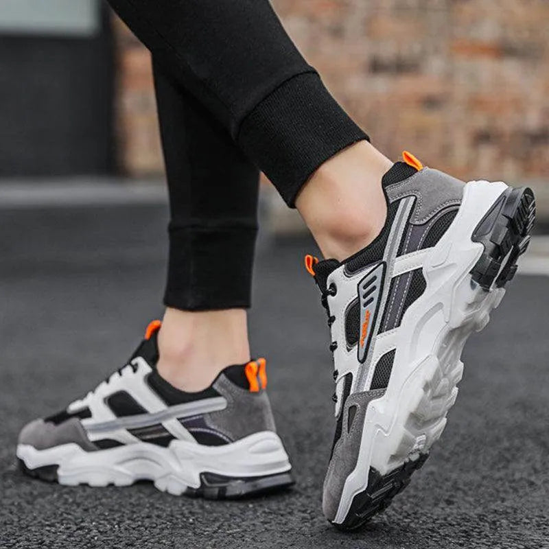 Person wearing gray and black sneakers with orange accents on a blurred street background