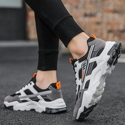 Person wearing gray and black sneakers with orange accents on a blurred street background