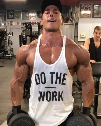 Muscular man in a gym wearing a tank top with 'DO THE WORK' text