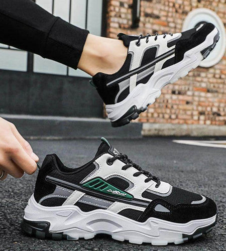 Black and white sneakers with green accents worn by a person on a street.