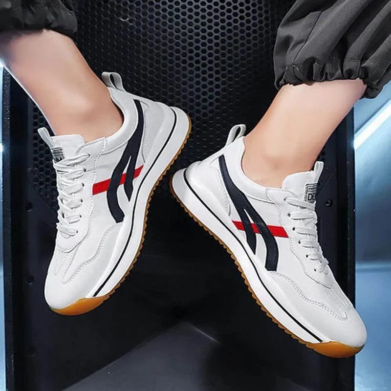 White sneakers with red and black accents worn by a person sitting on a black chair.