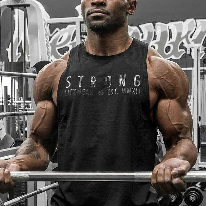 Muscular man lifting weights in a gym wearing a black tank top with 'STRONG' printed on it.