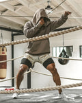 Person in a gray hoodie and shorts standing in a boxing ring with ropes.