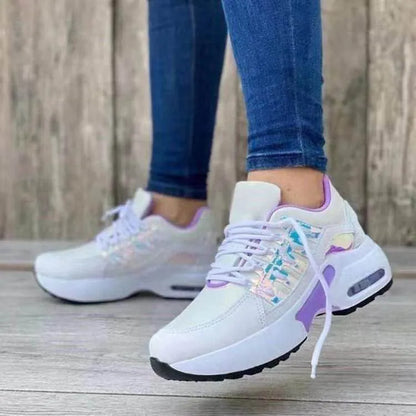 White sneakers with colorful accents worn by a person on a wooden floor.