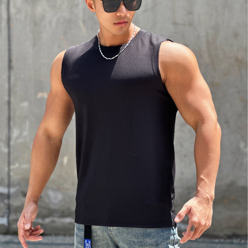 Man wearing a black sleeveless shirt and sunglasses against a gray wall.