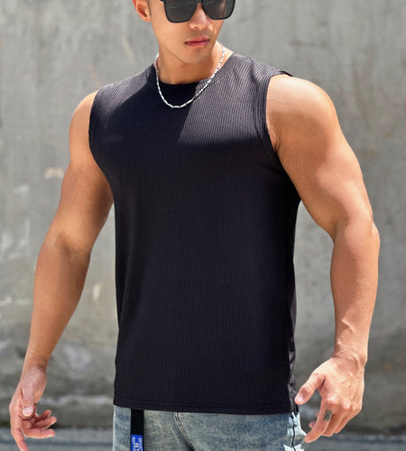 Man wearing a black sleeveless shirt and sunglasses against a gray wall.
