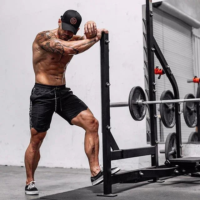 Muscular man in black shorts and cap exercising with weights in a gym.