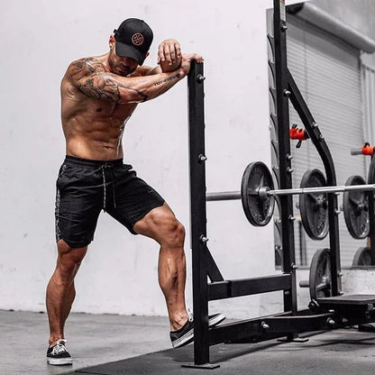 Muscular man in black shorts and cap exercising with weights in a gym.