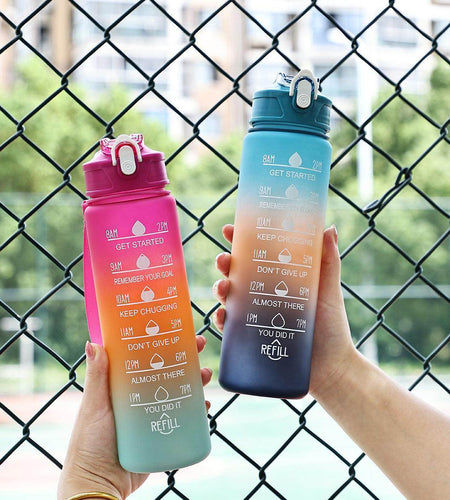 Two motivational water bottles held by hands against a chain-link fence.