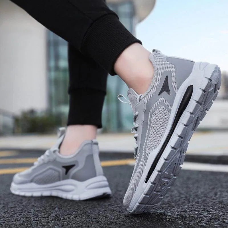 Gray athletic shoes worn outdoors on a pavement.