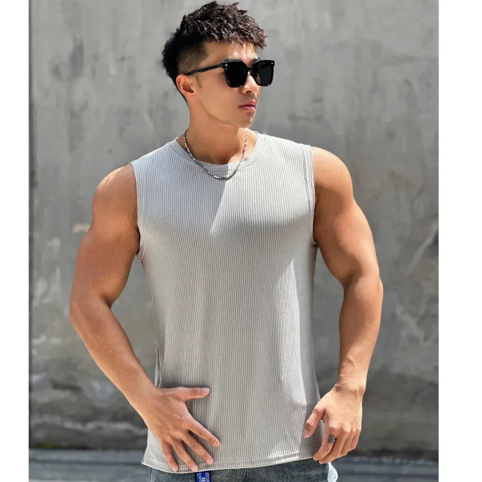 Man wearing a gray tank top and sunglasses against a concrete wall.