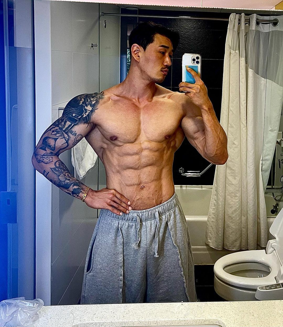 Man taking a mirror selfie in a bathroom, wearing gray sweatpants.