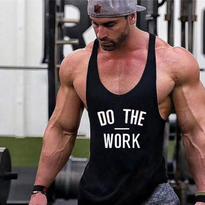 Muscular man wearing a black tank top with 'DO THE WORK' text in a gym setting