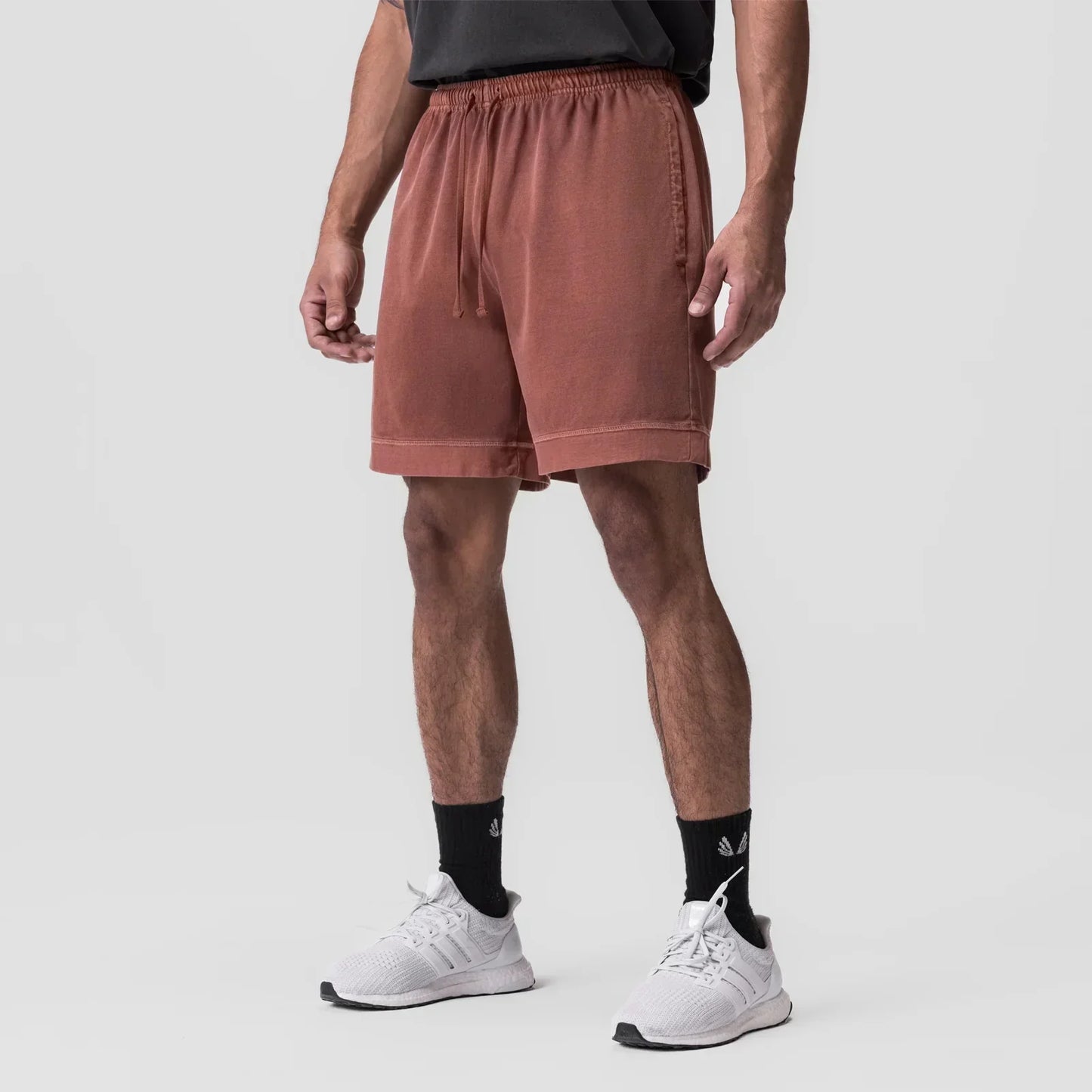 Person wearing brown shorts and white sneakers on a light gray background