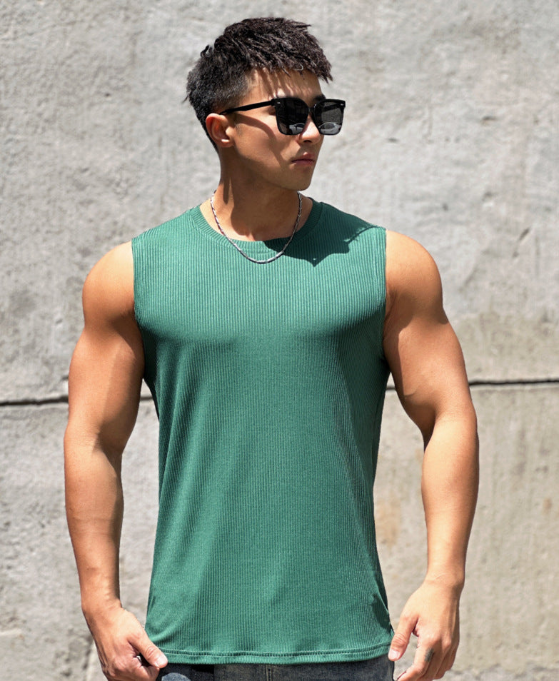 Man wearing a green tank top and sunglasses against a gray wall.