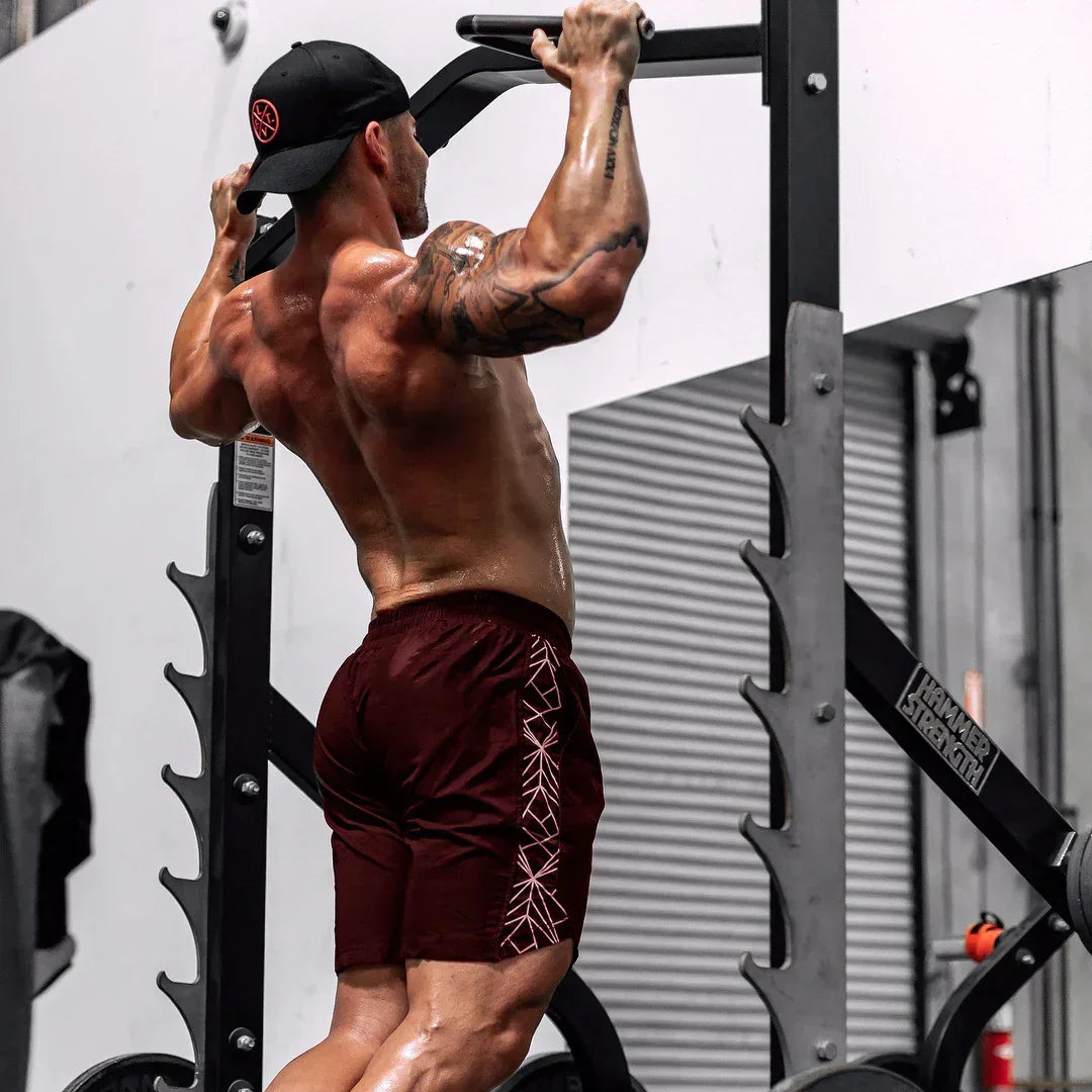 Muscular man performing pull-ups on a pull-up bar in a gym setting.