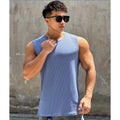 Man wearing a blue tank top and sunglasses against a gray wall.