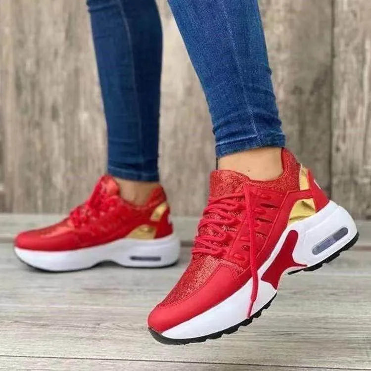 Red sneakers with gold accents worn with blue jeans on a wooden floor.