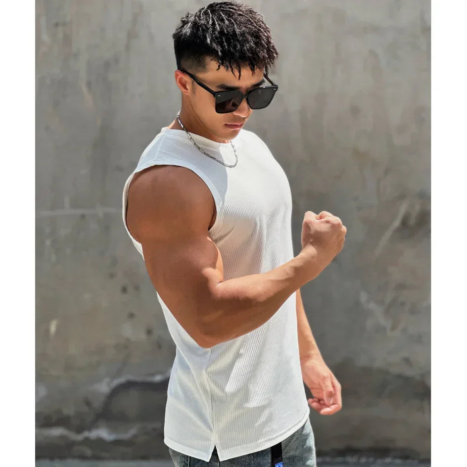 Man flexing his arm in a white sleeveless shirt against a gray wall