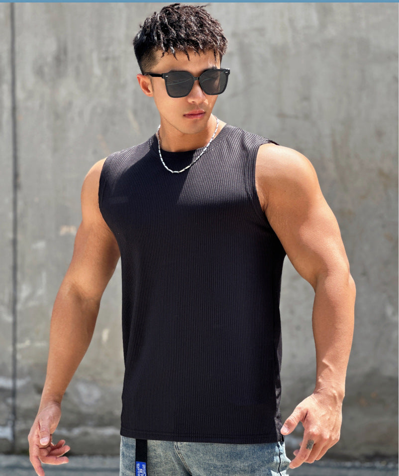 Man wearing a black sleeveless shirt and sunglasses against a gray wall.