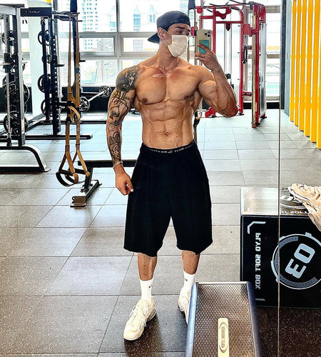 Muscular man in a gym wearing a face mask, black shorts, and white sneakers.