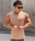 Man wearing a beige tank top and sunglasses against a textured wall.