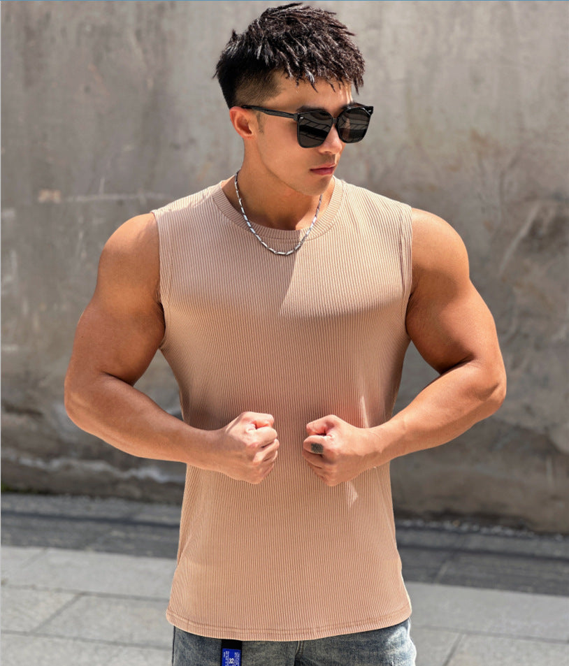 Man wearing a beige tank top and sunglasses against a textured wall.