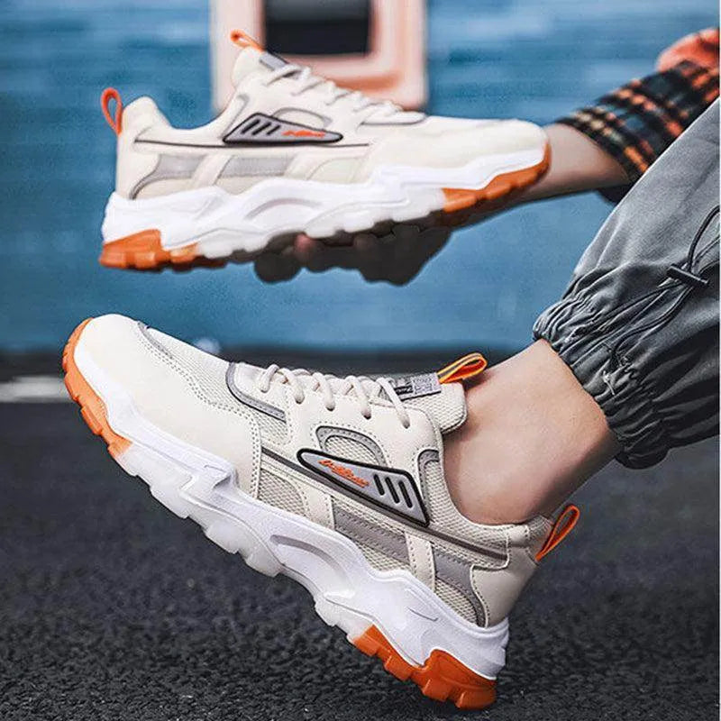 Beige and orange sneakers worn by a person sitting on a dark surface with a blurred blue background.