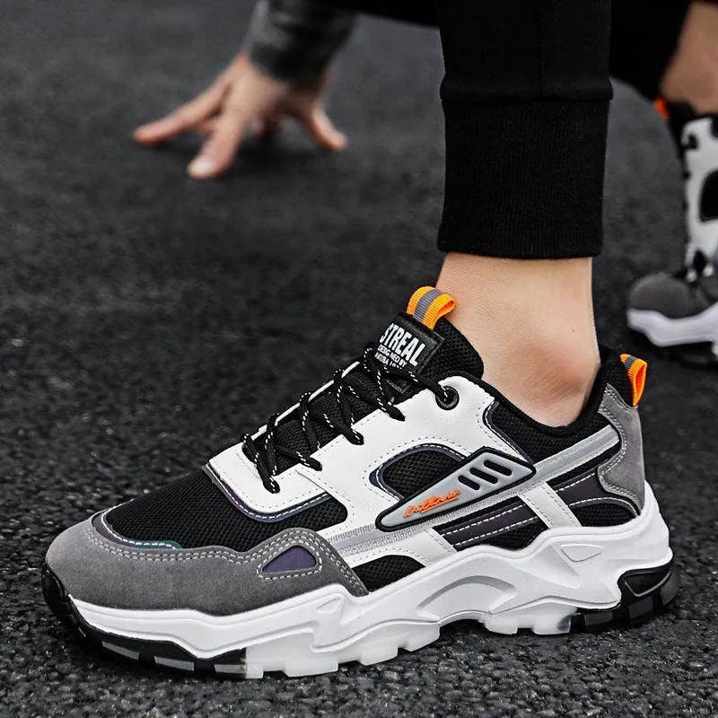 Person wearing black and gray sneakers with orange accents on a dark surface