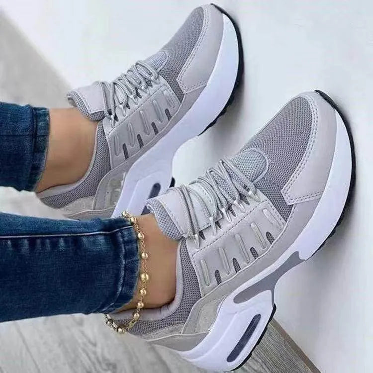 Gray sneakers with white soles worn by a person on a light gray background